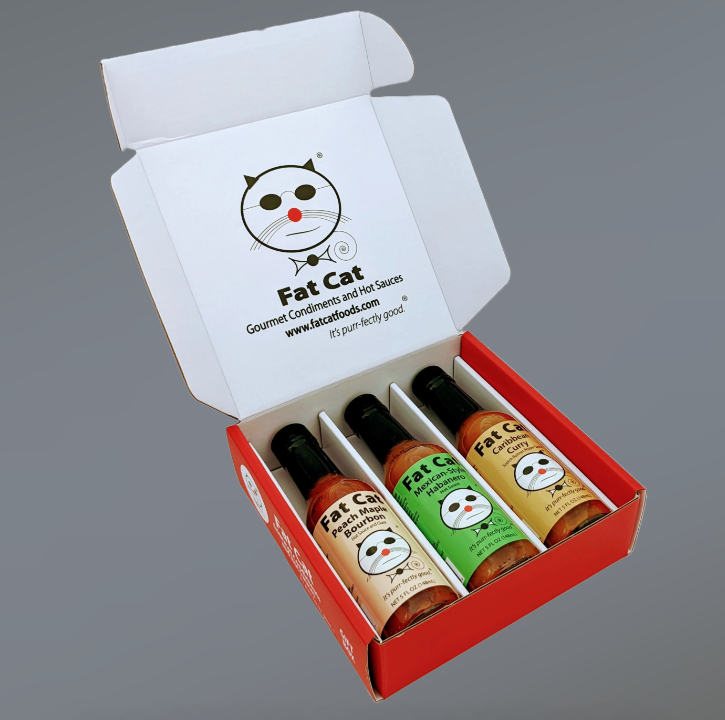 Box of Fat Cat Gourmet Condiments with four bottles on a gray background